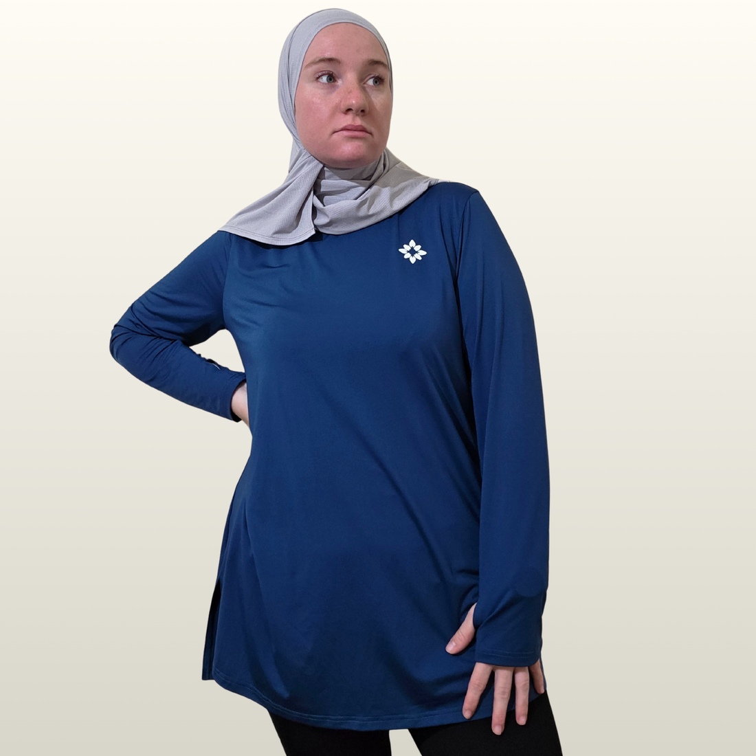 Woman wearing a blue long-sleeve top with a logo on a plain background