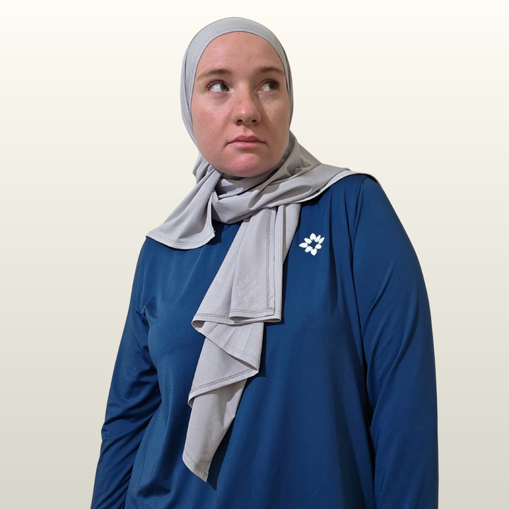 Person wearing a blue top and gray hijab with a white brooch on a beige background