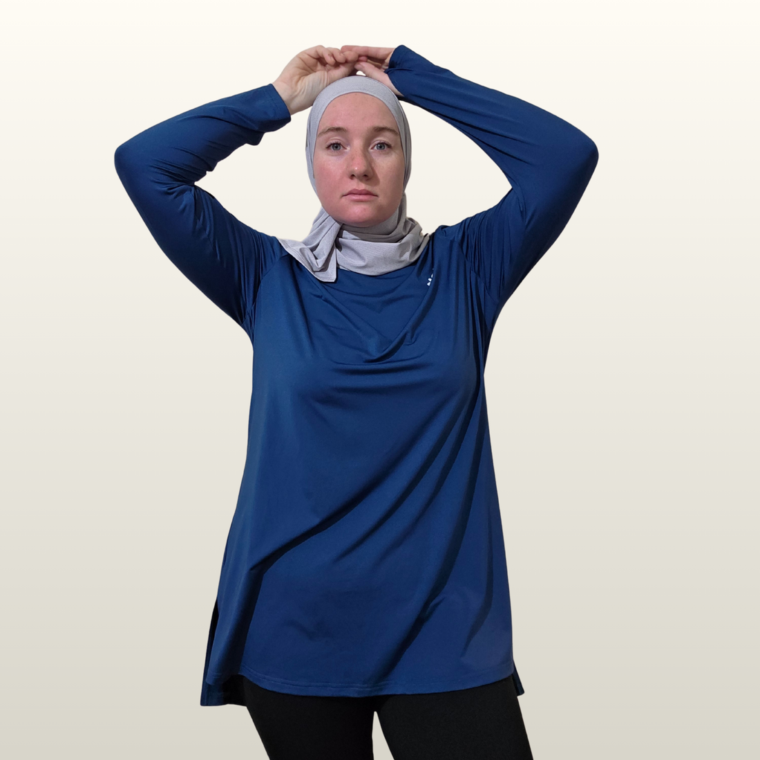 Person wearing a blue long-sleeve top and a hijab on a plain background